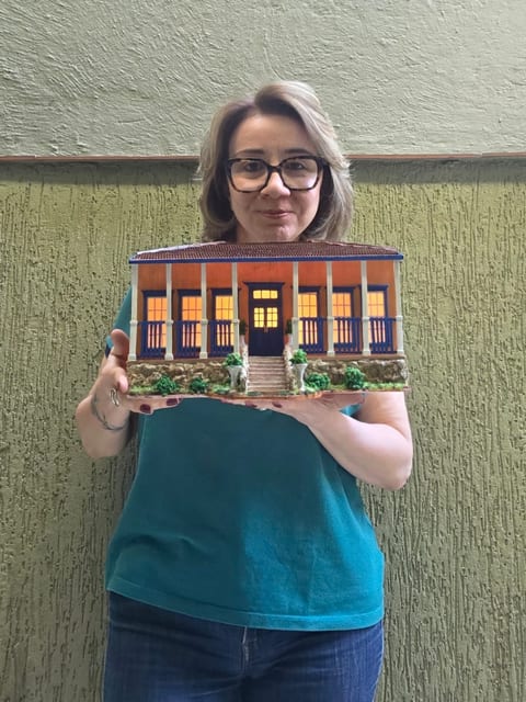 Tarcila Biffi segurando uma réplica de casa de fazenda em miniatura.