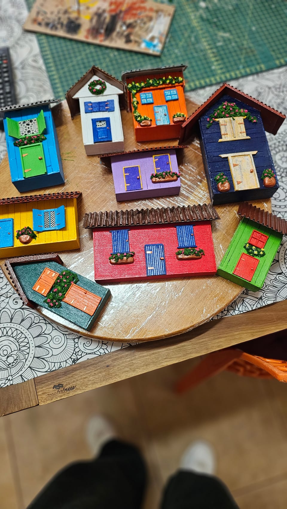 Casinhas coloridas em miniatura feitas com palitos de madeira, com portas, janelas e floreiras — conjunto sobre a mesa