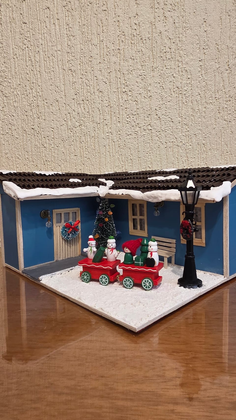 Diorama de Natal de uma casa azul com telhado nevado e um trenzinho vermelho com bonecos de neve — vista em ângulo