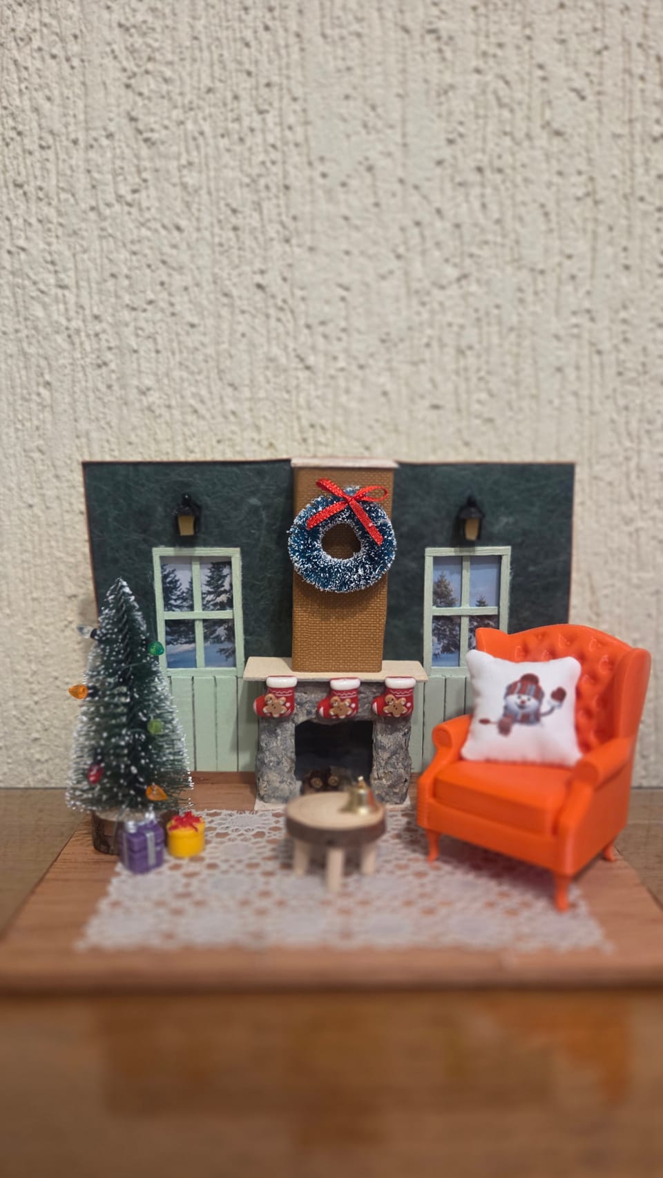 Diorama de Natal com paredes verde-escuras, lareira com guirlanda, poltrona laranja e árvore com presentes — vista frontal