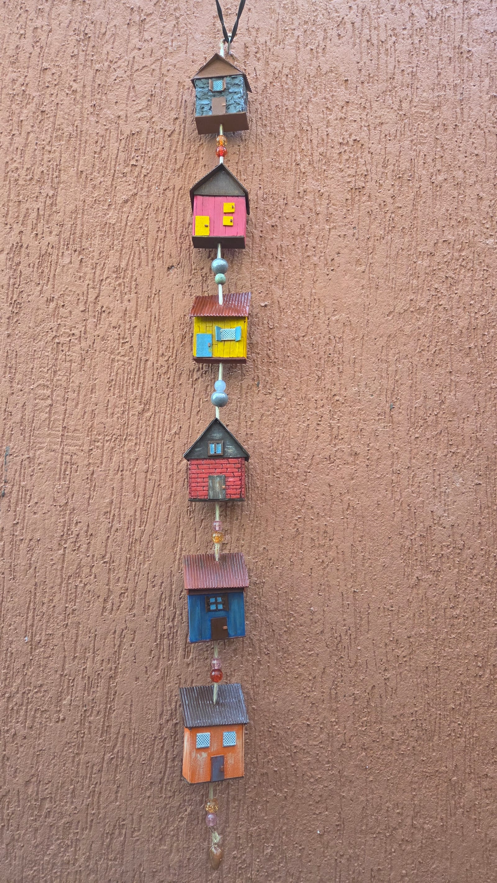 Móbile vertical de casinhas coloridas penduradas, em rosa, amarelo, vermelho, azul e laranja — vista inteira