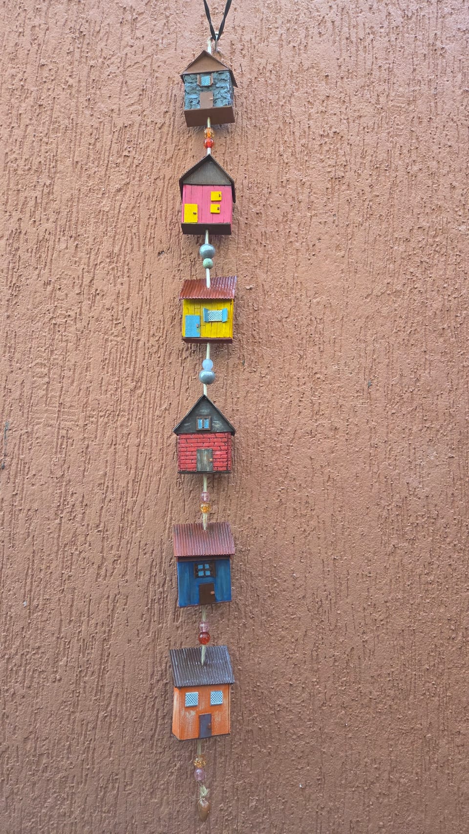 Móbile vertical de casinhas coloridas penduradas, em rosa, amarelo, vermelho, azul e laranja — vista inteira