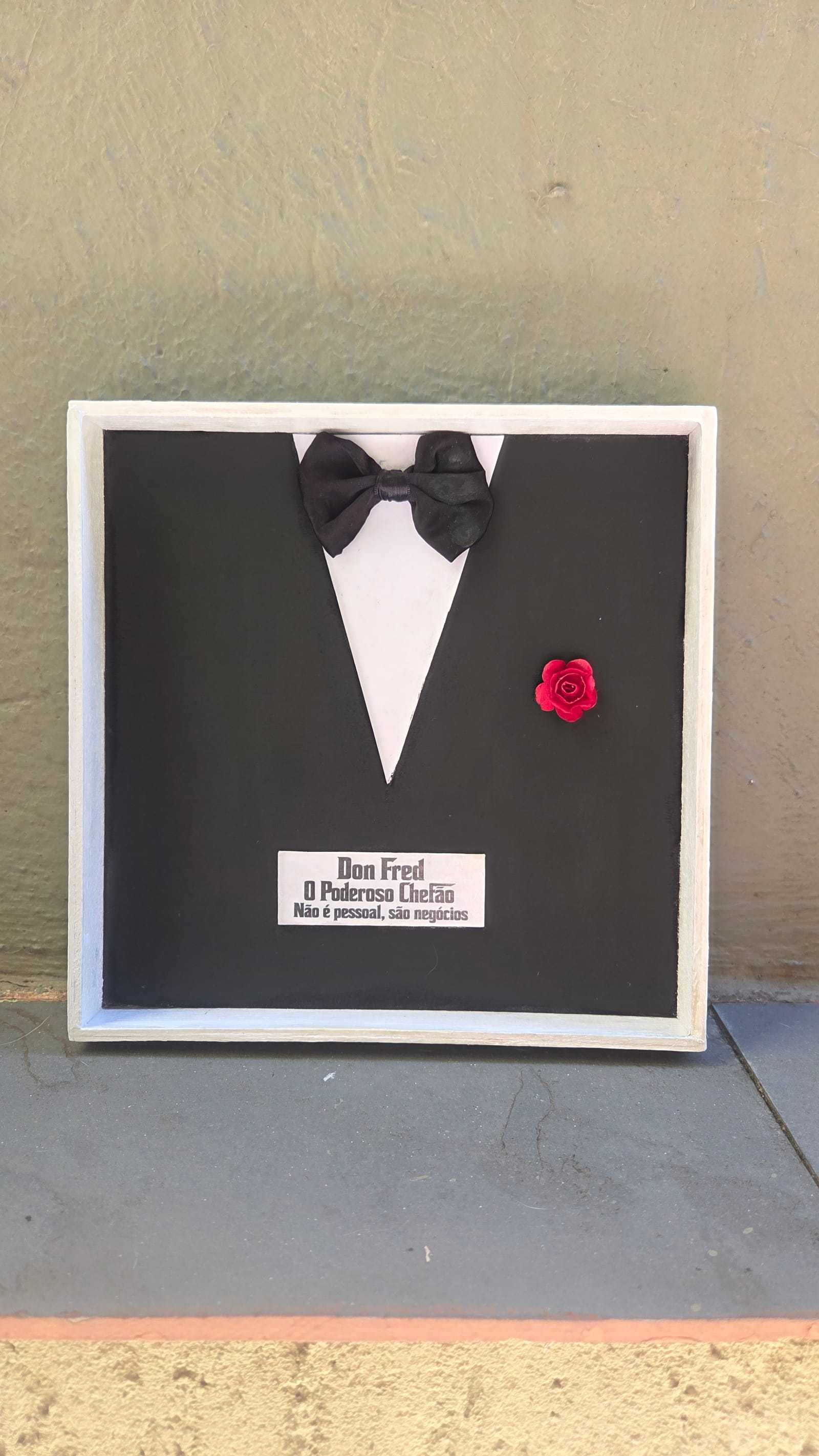 Quadro com smoking preto, camisa branca, gravata-borboleta, rosa vermelha e plaquinha personalizada — vista frontal