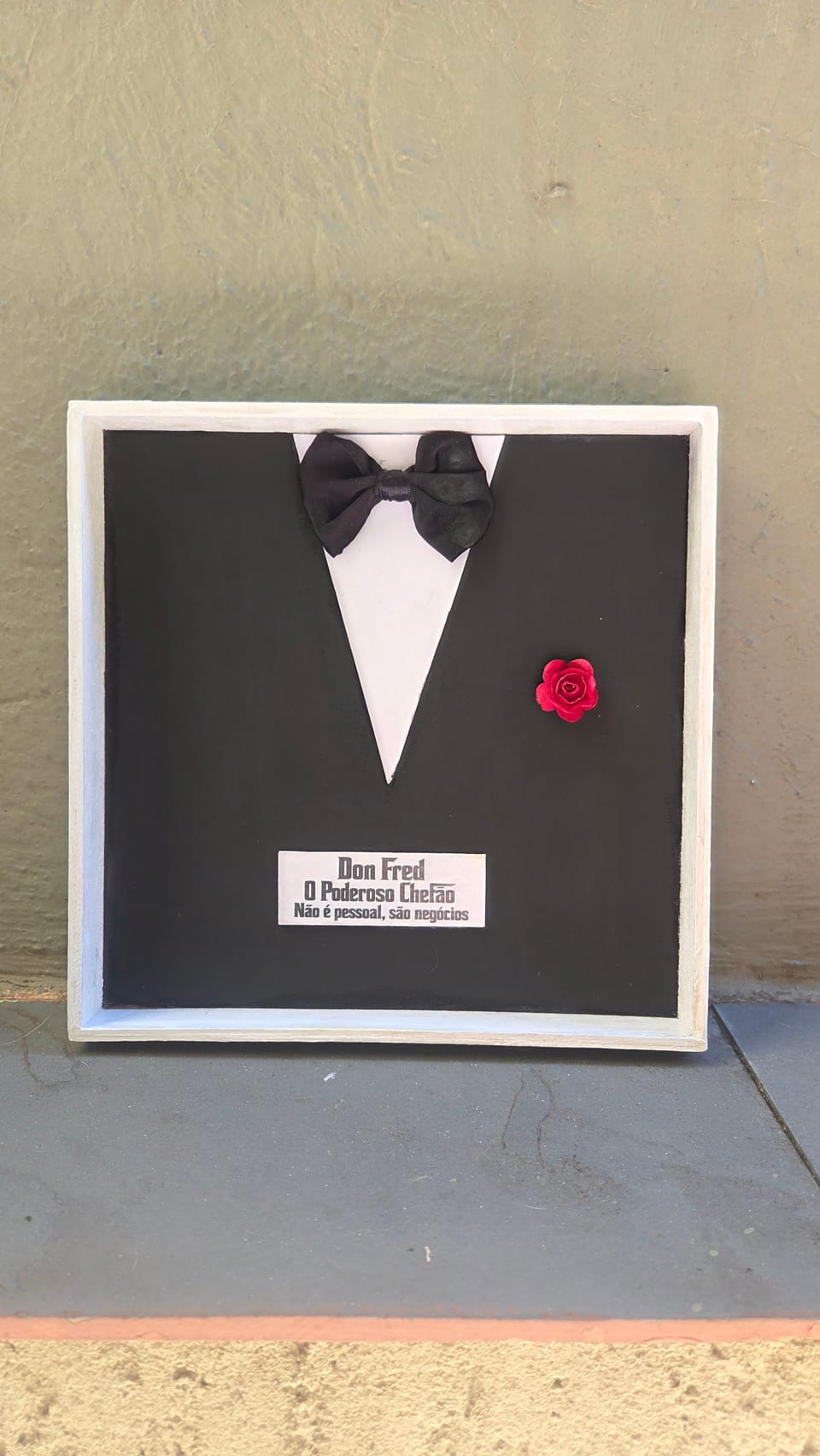 Quadro com smoking preto, camisa branca, gravata-borboleta, rosa vermelha e plaquinha personalizada — vista frontal