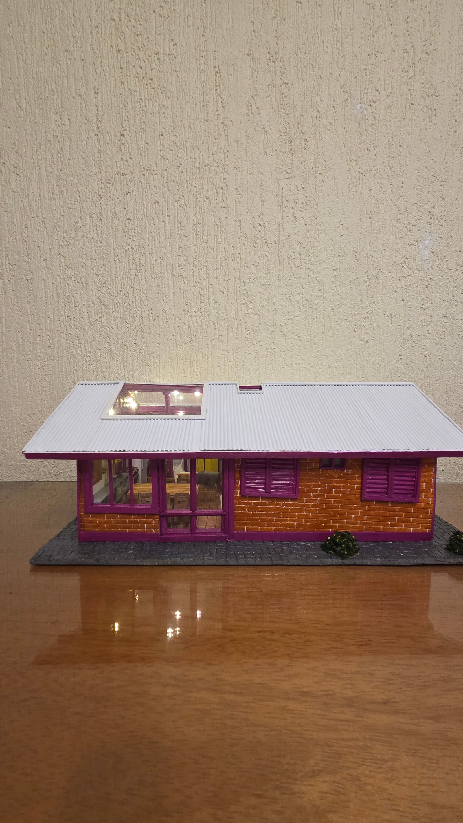 Réplica de casa térrea de tijolinhos com detalhes em vinho, telhado claro removível e interior mobiliado — vista frontal