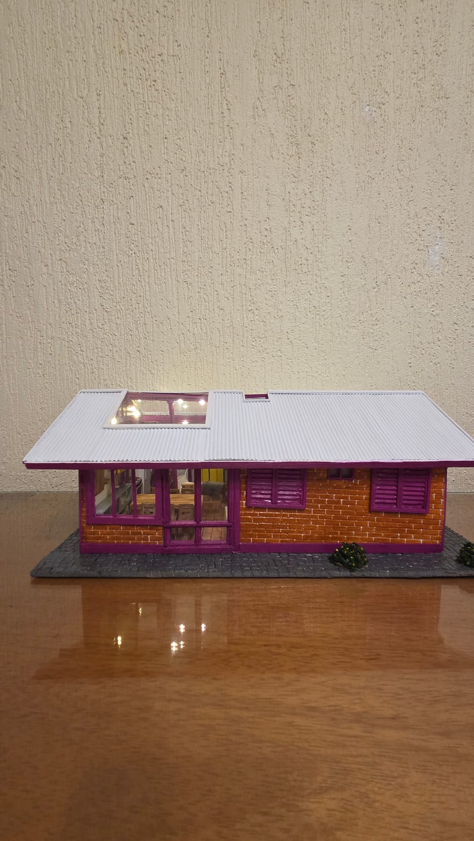Réplica de casa térrea de tijolinhos com detalhes em vinho, telhado claro removível e interior mobiliado — vista frontal